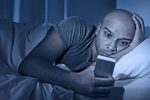 man staring at cell phone in bed