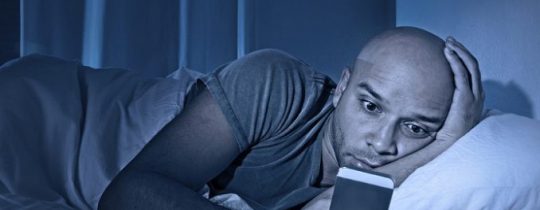 man staring at cell phone in bed