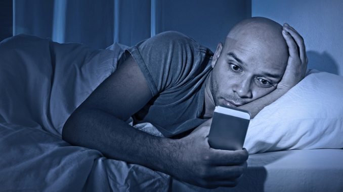man staring at cell phone in bed